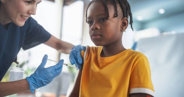 Parlak hastanedeki koltukta oturan ve çocuk felci aşısı olan genç Afrikalı Amerikalı çocuk. Kafkas Kadın Hemşire Enjeksiyon Yapıyor