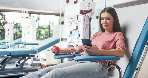 stock image Caucasian Woman Donating Blood For People In Need In Hospital. Female Donor Squeezing Heart-Shaped Red Ball To Pump Blood And Chatting Online Using