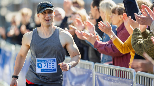 Портрет улыбающегося мужчины средних лет, бегущего в городском марафоне, машущего вспомогательной аудитории. Дружелюбный счастливый мужчина-бегун