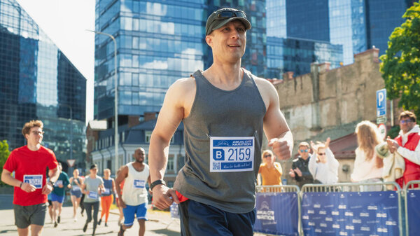 Портрет улыбающегося мужчины средних лет, бегущего в городском марафоне, машущего вспомогательной аудитории. Дружелюбный счастливый мужчина-бегун