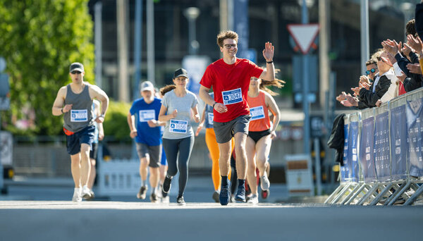 Съемки группы людей, бегущих в марафоне и машущих своим любимым и сторонникам в аудитории. Бегунья в длину