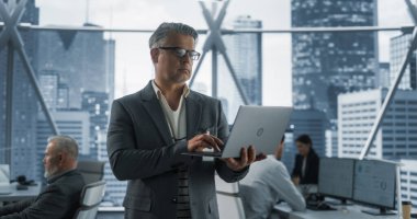 Şehir merkezindeki gökdelende çeşitli çalışanlarla Ofiste Yürüyen başarılı beyaz iş adamı. E 'de Dizüstü bilgisayar kullanan Orta Çağ Girişimcisi