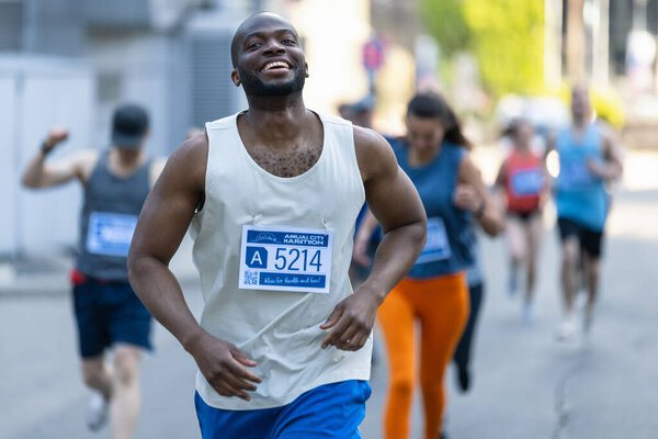 Портрет улыбающегося молодого чернокожего человека, бегущего в городском марафоне, машущего вспомогательной аудитории. Дружелюбный счастливый мужчина-бегун