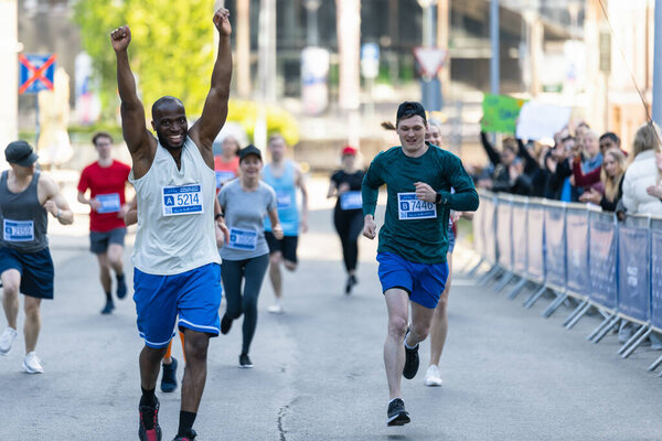 Портрет улыбающегося молодого чернокожего человека, бегущего в городском марафоне, машущего вспомогательной аудитории. Дружелюбный счастливый мужчина-бегун