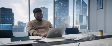 Başarılı siyahi iş adamının portresi büyük ofisindeki dizüstü bilgisayarda çalışıyor. Gülümseyen Dijital Girişimci E için Veri Analizi Yapıyor