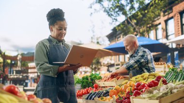 Afrika Çiftçi Pazarı Yöneticisi şehir meydanında Taze Doğal Tarım Ürünleri satan satıcılarla birlikte dizüstü bilgisayar kullanıyor. Orta Çağ Siyah