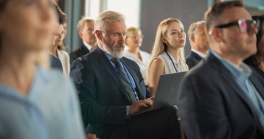 Kalabalıkta oturan ve Uluslararası Teknoloji Konferansında dizüstü bilgisayar kullanan kıdemli erkek üst düzey yönetici. Keynote Dinleyen Beyaz Adam