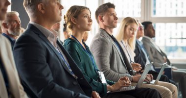 Young Woman Sitting in Crowded Audience at a Business Conference. Female Delegate Smiling, Using Laptop Computer. Manager Watching Motivational clipart