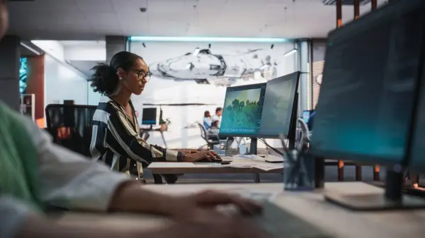 stock image Black Female Game Developer Using Desktop Computer With 3D modelling Software And Talking to Asian Female Project Manager in Game Design Studio Office