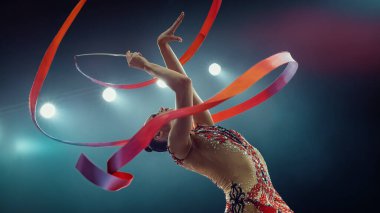 Parlak Kostümlü Asyalı Kadın Jimnastikçi, Parlak Stadyum Işıkları Altında Zarif Manevra Kurdelesi, Sanatsal Yeteneği ve Hassasiyeti