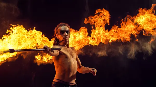 stock image Shirtless Male Fire Performer With Dreadlocks Wields Flaming Staff, Creating Mesmerizing Display of Fire and Sparks Against Dark Background, His