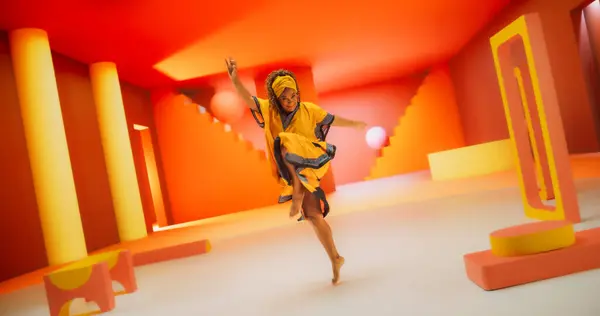 stock image Beautiful Black Woman in African Outfit Dancing Energetically in Geometric Abstract Orange Environment. Creative Female Performing Dance Choreography