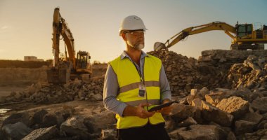 Caucasian Male Civil Engineer Wearing Protective Goggles And Using Tablet On Construction Site On A Sunny Day. Man Inspecting Building Progress clipart