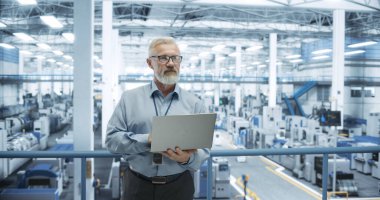 Deneyimli Erkek Mühendis Platform 'da duruyor, Dizüstü bilgisayar kullanıyor ve Modern Otomatik Elektronik Üretiminde