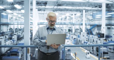 Kıdemli Fabrika Yöneticisi, özerk yapay zeka robotlarıyla birlikte bir Fütüristik Endüstriyel Üretim 'de dizüstü üzerinde çalışıyor. Tüm Verileri İzleyen Uzman