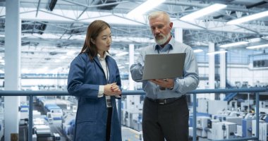 Deneyimli Erkek ve Kadın Mühendisler Bir Platformda Duruyor, Laptop Bilgisayarı ve Modern Otomatik Elektronik Prodüksiyon Kullanıyor