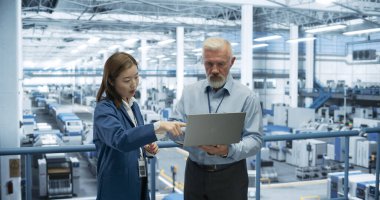 Erkek Mühendis ve Kadın Proje Yöneticisi Bir Platformda Duruyor, Konuşuyor, Dizüstü bilgisayar kullanıyor ve Modern Otomatik Yapım 'da İzliyor