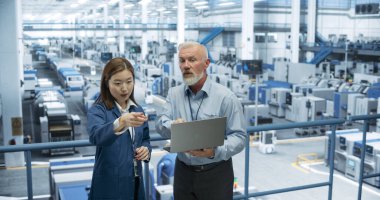 Orta Çağ Mühendisi ve Genç Japon Teknisyen Laptop Bilgisayar kullanıyor. Şartları İzleyen, Analiz eden Uzmanlar