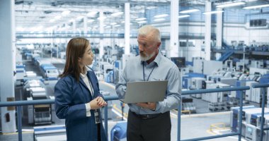 Teknoloji fabrikasında çalışan Endüstriyel Mühendisler. Beyaz adam ve Japon kadın dizüstü bilgisayar kullanıyor ve iletişim kuruyor. Bir portre