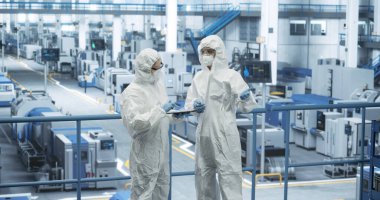 Üretim fabrikasında tam vücut polipropilen kaplama giyen kadın işçiler var. Tablet Bilgisayar Kullanan Uzmanlar Otomatik Çalışmayı Tartışıyor