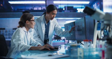 Tıbbi Araştırma Merkezi 'nde konuşan Asyalı ve Kafkas kadın doktorlar ve MRI beyin taramalarını analiz etmek için masaüstü bilgisayarı kullanıyorlar. Cerrah ve