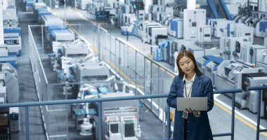 Asyalı Kadın Mühendis Bir Fabrika Tesisinde duruyor, Dizüstü bilgisayar üzerinde çalışıyor, Elektronik Üretim Teknolojileri Araştırıyor ve Geliştiriyor