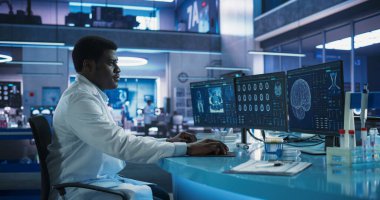 Siyah Erkek Nörobilimci, Tıbbi Araştırma Merkezi 'ndeki MRI taramalarını analiz etmek için Masaüstü Bilgisayarını kullanıyor. Afrikalı Doktor CT taraması yapıyor