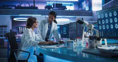 Tıbbi Araştırma Merkezi 'nde konuşan Asyalı ve Kafkas kadın doktorlar beyin tomografisini incelemek için masaüstü bilgisayarını kullanıyorlar. Cerrah ve Nörobilimci