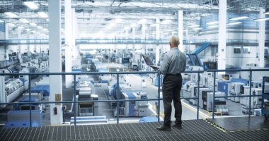 Deneyimli Erkek Mühendis Platform 'da duruyor, Dizüstü bilgisayar kullanıyor ve Modern Otomatik Elektronik Üretiminde