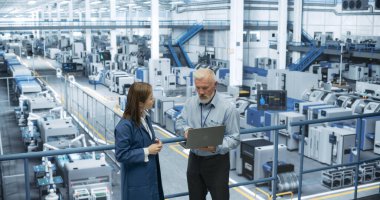 Erkek Mühendis ve Kadın Proje Yöneticisi Bir Platformda Duruyor, Konuşuyor, Dizüstü bilgisayar kullanıyor ve Modern Otomatik Yapım 'da İzliyor