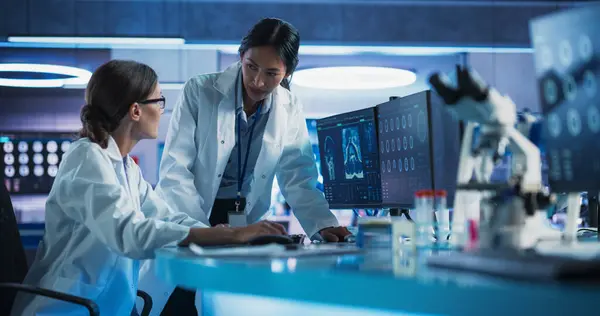 stock image Medical Hospital Research Laboratory: Caucasian And Asian Female Scientists Talking And Using Desktop Computer With MRI Scans Of Human Brain. Surgeon