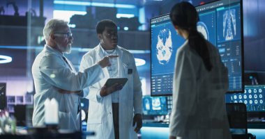 Tıbbi Nöroloji Hastanesi Laboratuar Toplantısı: Çeşitli Nöroşirüroloji ve Nörologlar Ekibi Televizyon Ekranı 'nı Analiz Ediyor, Beyin Görüntüleriyle MRI Taraması Yapıyor, Konuşuyor