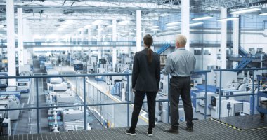 Erkek Mühendis ve Kadın Proje Yöneticisi Bir Platformda Duruyor, Konuşuyor, Dizüstü bilgisayar kullanıyor ve Modern Otomatik Yapım 'da İzliyor