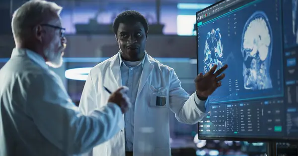 stock image Neuroscience Laboratory Meeting: Black Male Scientist And Caucasian Surgeon Discussing MRI Brain Scan On TV Display. Specialists Working On Medication