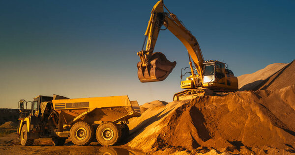 Строительная площадка в солнечный вечер: промышленный экскаватор погрузки песка в грузовик. Ход строительства нового микрорайона. Рабочие, работающие