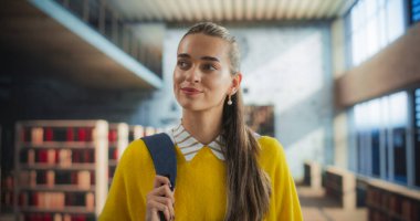 Üniversite Kampüsünde Kapalı Kapıda Yürüyen Mutlu Gülümseyen Genç Bir Öğrencinin Portresi. Sarı kazak giyen neşeli bir kadın, etrafına bakıyor.