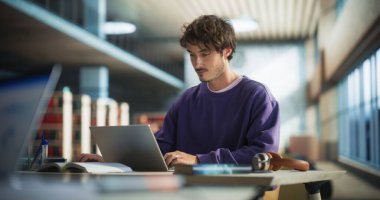 Bir dizüstü bilgisayarla üniversite egzersizinde çalışan şık bir erkek öğrencinin portresi. Çevrimiçi kolej kursunda okuyan yakışıklı bir genç.
