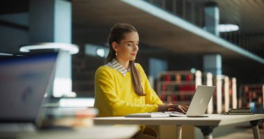 Sarı Jumper 'lı güzel beyaz kadın öğrenci dizüstü bilgisayarında okul tezi üzerinde çalışıyor. Çevrimiçi Çalışan Genç Zeki Kadın