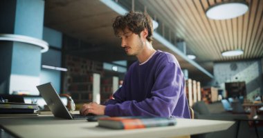 Modern Kütüphanede Öğrenci Çalışması. Genç Düşünen ve Sorunları Çözen Okul Egzersizleri. Üniversitede Çalışmak için Erkek Dizüstü Bilgisayarı Kullanıyor