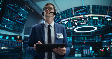 Başarılı bir Menkul Kıymetler Borsası Müdürünün Portresi. Kulaklık takıyor, Modern Ofiste Çalışıyor. Bir Tablet Bilgisayarda Proaktif Ticari Tarayıcı İnternet Taraması