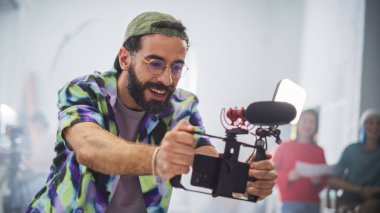 Sakallı ve gözlüklü genç Latin film yapımcısı, yoğun bir stüdyoda kamerayı neşe içinde çalıştırıyor, çeşitli takım üyeleriyle çevrelenmiş,