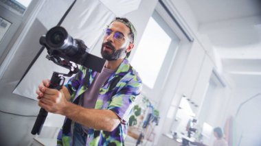 Odaklanmış Sakallı Genç Latin Videograf, Parlak Stüdyoda Çekim, Profesyonel Kamera, Modern Film Yapımı Ekipmanları ile çevrili