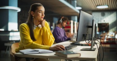 Halk kütüphanesinde çalışmak için Masaüstü Bilgisayarı kullanan düşünceli Avrupa Koleji Öğrencisi. Çevrimiçi Güzel Genç Kadın Öğreniyor, Hazırlanıyor