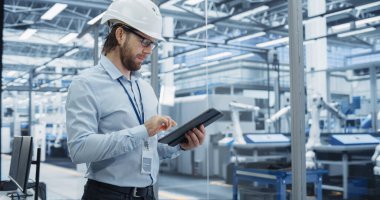 Elektronik Fabrikası Yöneticisi, Robotik Kollarla Endüstriyel Üretim 'de Tablet üzerinde çalışıyor. Hard Hat 'in Büyük Verileri İzleme Uzmanı