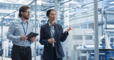 Modern bir Elektronik Fabrikasında Tablet Bilgisayar kullanarak Ofiste Yürüyen İki Çeşitli Mühendis. Kadın ve Erkek Uzmanlar Konuşuyor, İzliyor