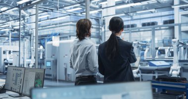 Genç beyaz mühendis ve Asyalı teknisyen sohbet ediyor ve dizüstü bilgisayar kullanıyor. Şartları İzleyen, Analiz eden Uzmanlar