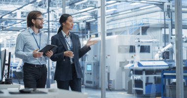 Ofiste yürüyen iki farklı mühendis, bir elektronik fabrikasında tablet bilgisayar kullanıyorlar. Kadın ve Erkek Uzmanlar Konuşuyor, Robotları İzliyor