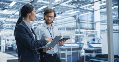 Neşeli Mühendis ve Mutlu Asyalı Bilimadamı Laptop ve Tablet Bilgisayarları Kullanıyor, Robotlarla Bir Fabrikada Konuşuyor