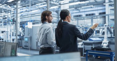 Genç beyaz mühendis ve Asyalı teknisyen sohbet ediyor ve dizüstü bilgisayar kullanıyor. Şartları İzleyen, Analiz eden Uzmanlar