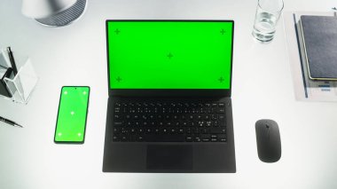 Üzerinde Şablon Chromakey Ekranı olan Smartphone 'un yanındaki Ofis Masasında duran Bir Dizüstü Bilgisayarın Üst Aşağı Görünümü